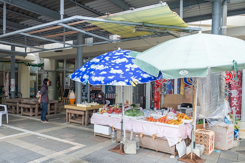 宮古島市公設市場|パラソルの建てられた野菜売り場とおばぁ。