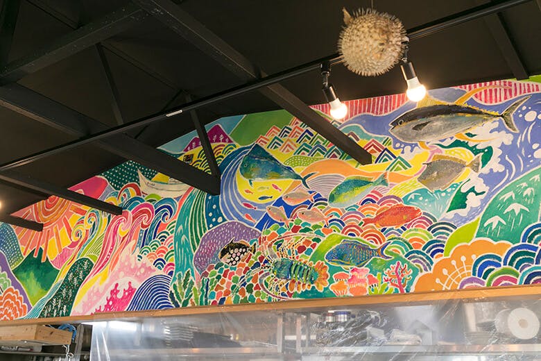 国頭港食堂(くにがみみなとしょくどう)|カウンター上に飾られた、絵本作家savaが描いた、やんばるを表現したエネルギッシュな壁画